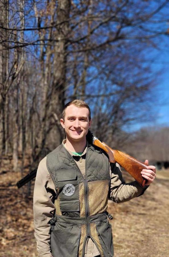 a man standing with a gun on his shoulder outside next to the woods